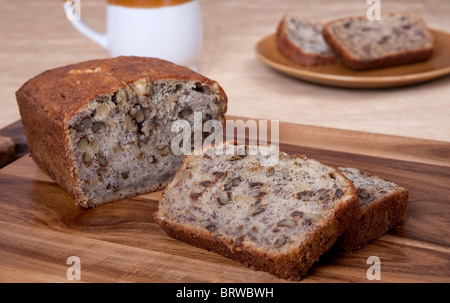 Pane a fette di banana pane alle noci su un tagliere con uno che serve di due fette e una tazza in background Foto Stock