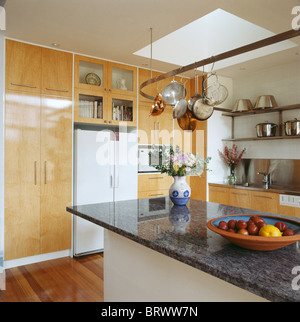 Il granito nero del piano su unità di isola in cucina moderna con grande stile americano e frigo-freezer e legno pallido montati armadi Foto Stock