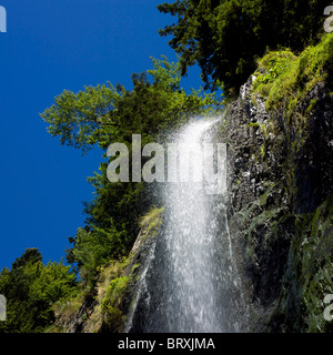 Maestosa cascata che scende dalla scogliera rocciosa sotto il cielo azzurro e lussureggianti alberi verdi, massiccio di Sancy, Puy-de-Dôme, regione d'Alvernia, Francia Foto Stock