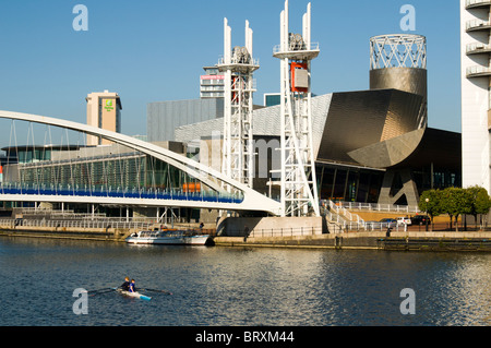 Due persone sculling (canottaggio) sul Manchester Ship Canal vicino al Lowry Arts Center, Salford Quays, Manchester, Regno Unito Foto Stock