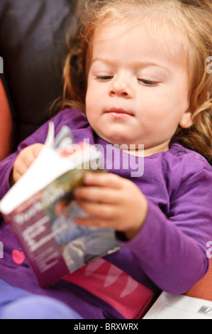 Un bambino ragazza rilassante su un divano legge una lingua turca libro di studio. Foto Stock