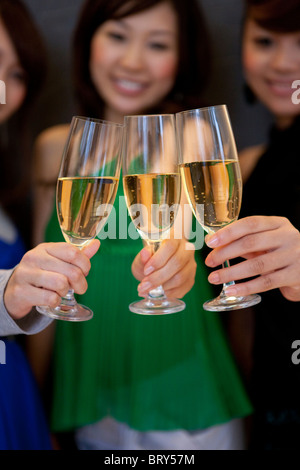 Tre giovani donne la tostatura con bicchieri di champagne, sfondo nero, la messa a fuoco del differenziale Foto Stock