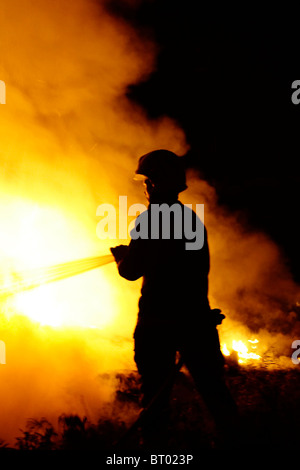 Silhouette di un vigile del fuoco che combatte contro un fuoco di notte Foto Stock