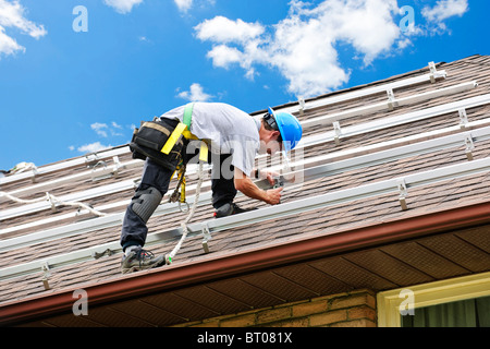 Uomo di installare guide per pannelli solari sulla casa residenziale tetto Foto Stock