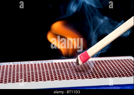 Un luci matchstick dopo che si è battuto contro la pietrina superficie di una scatola di confronto. Foto Stock