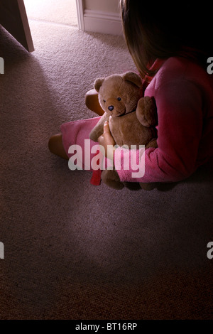 Bambina da solo in una stanza buia tenendo un orsacchiotto di peluche, in vista posteriore 3 Foto Stock