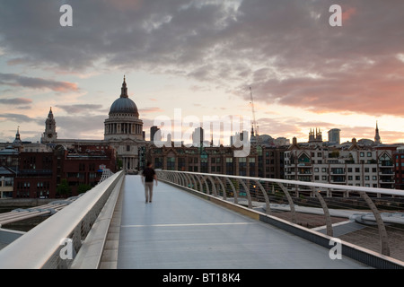 Uomo che cammina su Millennium Bridge sul fiume Tamigi all'alba guardando verso la Cattedrale di St Paul, Londra, Regno Unito Foto Stock