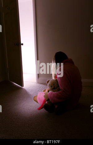 Bambina da solo in una stanza buia tenendo un orsacchiotto di peluche, in vista posteriore 5 Foto Stock