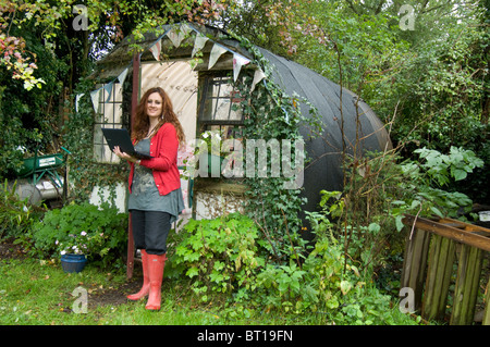 Woman in Red wellies al di fuori del suo ufficio di casa a un convertito WWII bomb shelter nel suo giardino sul retro. Foto Stock