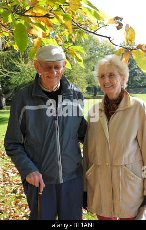 Due pensionati, una coppia di anziani, fuori su un autunno a piedi sorridenti con foglie d'oro sugli alberi Foto Stock