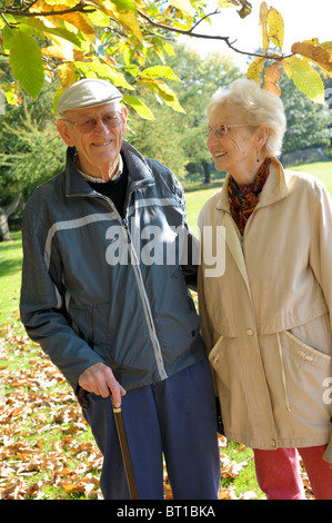 Due pensionati, una coppia di anziani, fuori su un autunno a piedi sorridenti con foglie d'oro sugli alberi Foto Stock