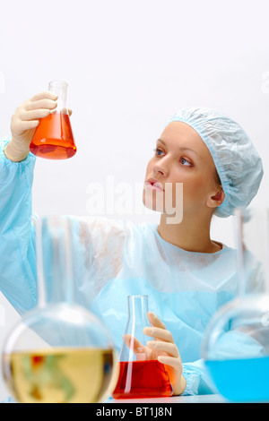 Graziosa assistente guardando il tubo di vetro con un liquido durante la prova medica Foto Stock