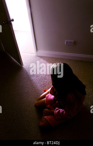 Ragazza seduta in una stanza buia, vista posteriore alla ricerca di una porta aperta in cui flussi di luce a. Foto Stock