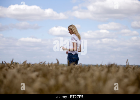 Una donna in piedi in un wheatfield, tenendo in mano una spiga di grano Foto Stock