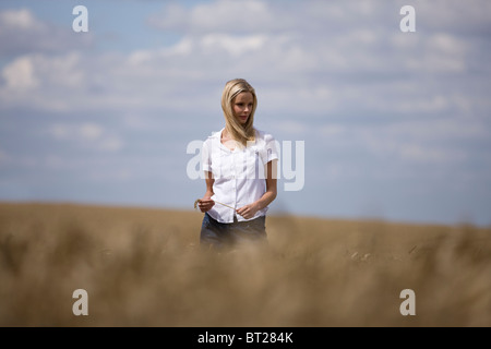 Una donna in piedi in un wheatfield, tenendo in mano una spiga di grano Foto Stock