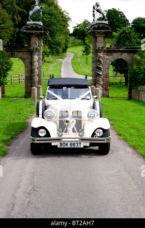 Un classico bianco auto nozze entra nel terreno di un inglese maestosa casa per un matrimonio. Foto Stock