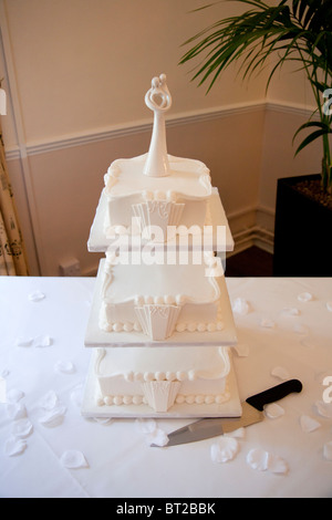 Una torta nuziale bianca a tre piani in stile Art Deco degli anni '1930 in mostra a un ricevimento nuziale, con dettagli glassati e un moderno top per sposa e sposo Foto Stock
