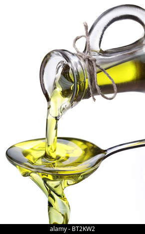 Olio d'oliva che fluisce dalla caraffa in cucchiaio isolate su un bianco. Foto Stock