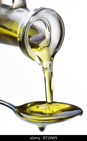 Olio d'oliva che fluisce dalla caraffa in cucchiaio isolate su un bianco. Foto Stock
