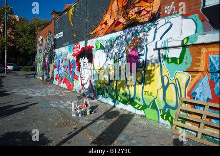 Muro di mattoni coperto di graffiti che mostra una testa maschio con le lattine in primo piano, Monaco di Baviera, Germania Foto Stock