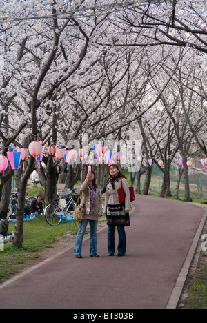 Due amici a prendere una foto dei fiori di ciliegio mentre godendo Hanami Foto Stock