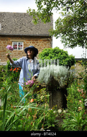 Una donna a caccia di fiori in un piccolo giardino cottage Oxfordshire UK Foto Stock