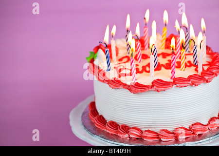 Torta di compleanno con candele accese su una piastra su sfondo rosa Foto Stock