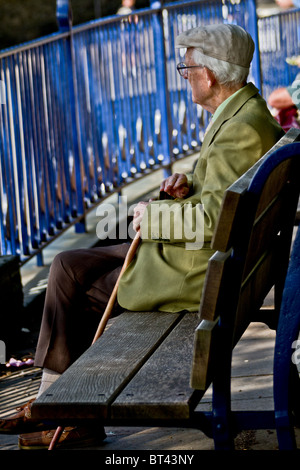 Anziano gentiluomo seduto su una panca in legno guardando avanti di lui, attraverso ringhiere blu Foto Stock
