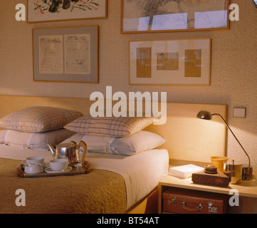 Le immagini sulla parete sopra il letto con cuscini e vassoio di prima colazione in camera da letto casa cittadina con la lampada accesa sul comodino Foto Stock