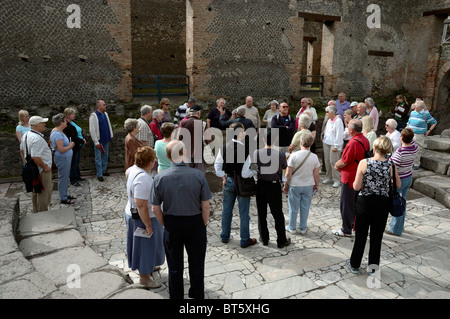 Tour guida per spiegare ai turisti lo scopo delle porte nella parete posteriore della fase dell'Odeion, Pompei, Italia Foto Stock