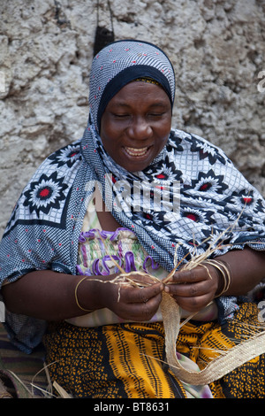 Jambiani, Zanzibar, Tanzania. Donna che fa una cinghia da un intreccio di erba. Foto Stock