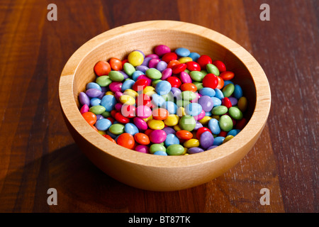 Cioccolato colorato fagioli in ciotola di legno su un tavolo di legno Foto Stock