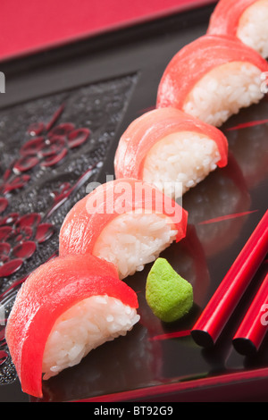 Rosso fresco di tonno nigiri sushi con bacchette rosso su un di legno intagliato con vassoio bright green wasabi Foto Stock