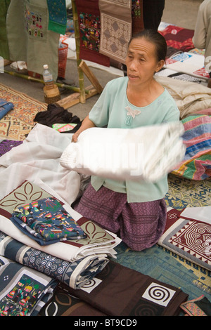 Una donna che offrono i tessuti di cotone in vendita presso il mercato notturno che riprende la strada principale di Luang Prabang da 5-11pm Notte Foto Stock