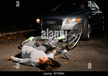 Temibile uomo in macchina si fermò a guardare a caduta di una giovane donna ciclista dopo una collisione sulla strada dopo un incidente di notte Foto Stock