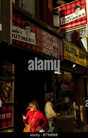 Una donna passa il fumo Poutinerie su Queen Street West in Toronto. Poutine, un cibo preferito in Québec, è in Toronto, troppo. Foto Stock