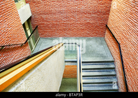 Prospettiva verso il basso sulla scala di un edificio realizzato in rosso arancio mattoni, materiali differenti su tutte le superfici. Foto Stock