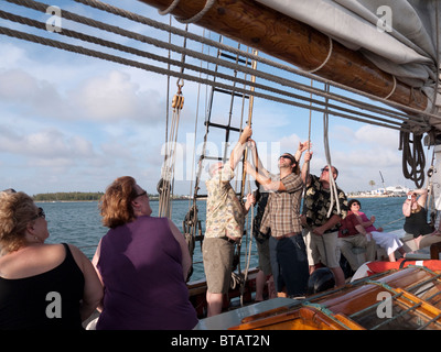 Passeggeri contribuendo a issare la vela sulla nave a vela la goletta Appledore off Key West in Florida USA Foto Stock