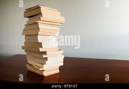 Una grande pila di libri si siede su una scrivania di legno con lo spazio vuoto dietro Foto Stock