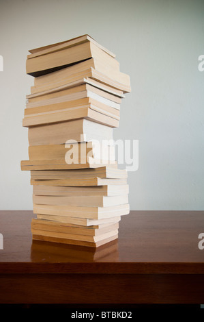 Una grande pila di libri si siede su una scrivania di legno con lo spazio vuoto dietro Foto Stock