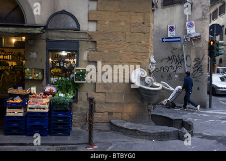 Uomo che cammina lungo il marciapiede vicino negozio locale su un angolo di Firenze angolo di strada Foto Stock