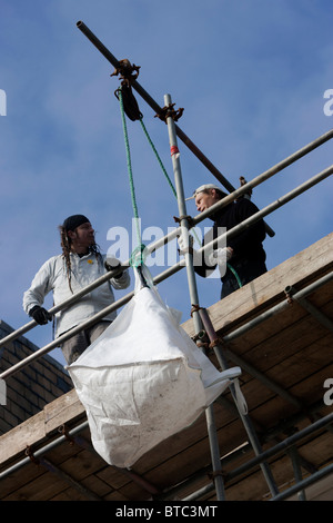 Due costruttori mostrato operante una puleggia sistema con funi mentre lavora su un edificio in Brighton, East Sussex, Regno Unito. Foto Stock