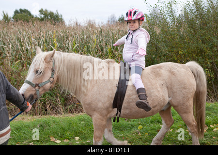 Piccola ragazza a cavallo di un pony con le braccia aperte Foto Stock