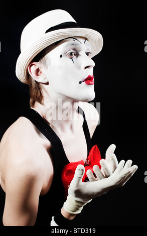 Mime con fiocco rosso in un cappello bianco e guanti a strisce su sfondo nero Foto Stock