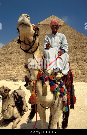Uomo arabo vestito in costumi tradizionali e turbante sulla sua testa seduto su un cammello di fronte a una piramide Foto Stock