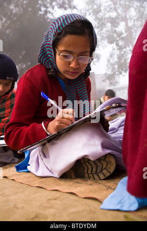 In un punjabi scuola rurale, bambini esami seduti sulle stuoie sul terreno aperto del cortile della scuola in mezzo ai resti di co Foto Stock