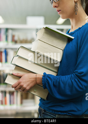 Donna che mantiene pila di libri in biblioteca Foto Stock