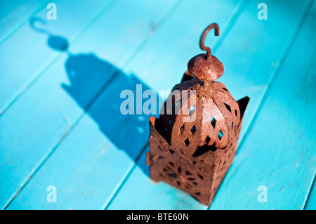 Un arrugginito Lanterna da esterno si siede al sole su un blu Tavolo da giardino. Foto Stock