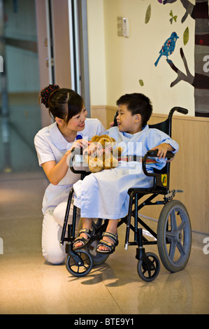 L'infermiera di parlare con un giovane bambino paziente in sedia a rotelle in corridoio in ospedale unità di pediatria Foto Stock