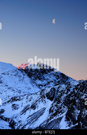 Luna e la prima alba rosa della luce solare sullo Scafell in inverno nel Lake District inglese Foto Stock